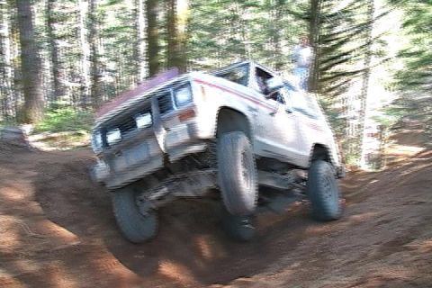 1996 Ford Bronco - A white SUV with a red stripe navigates a steep dirt trail in a wooded area.