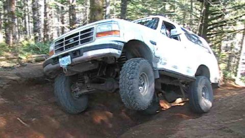 1996 Ford Bronco - White Ford Bronco navigates a challenging off-road trail through a wooded area.
