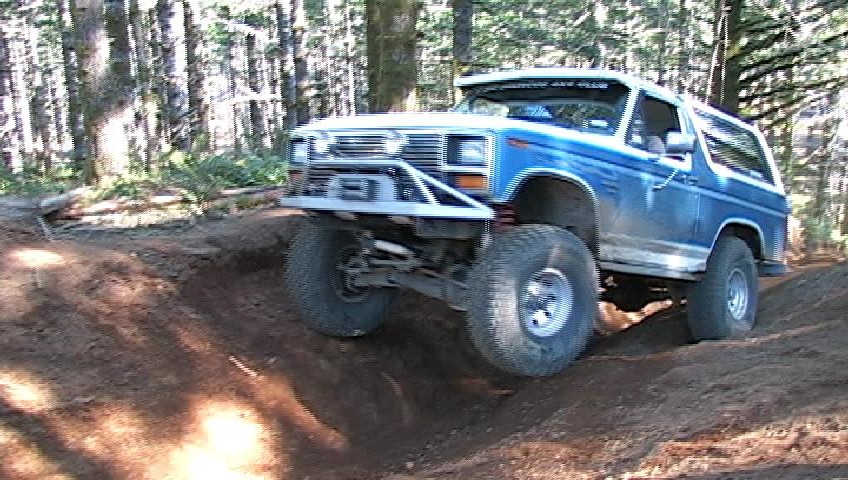 Lifted blue and white Ford Bronco on a dirt off-road trail in the woods