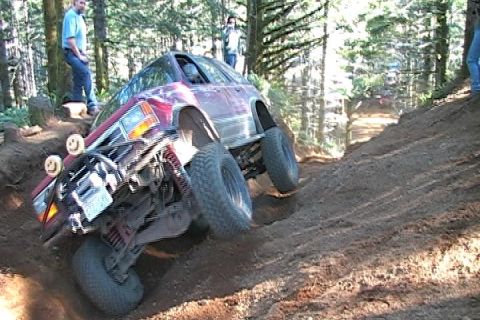 1996 Ford Bronco - Two off-road vehicles navigate a challenging dirt trail in a wooded area.