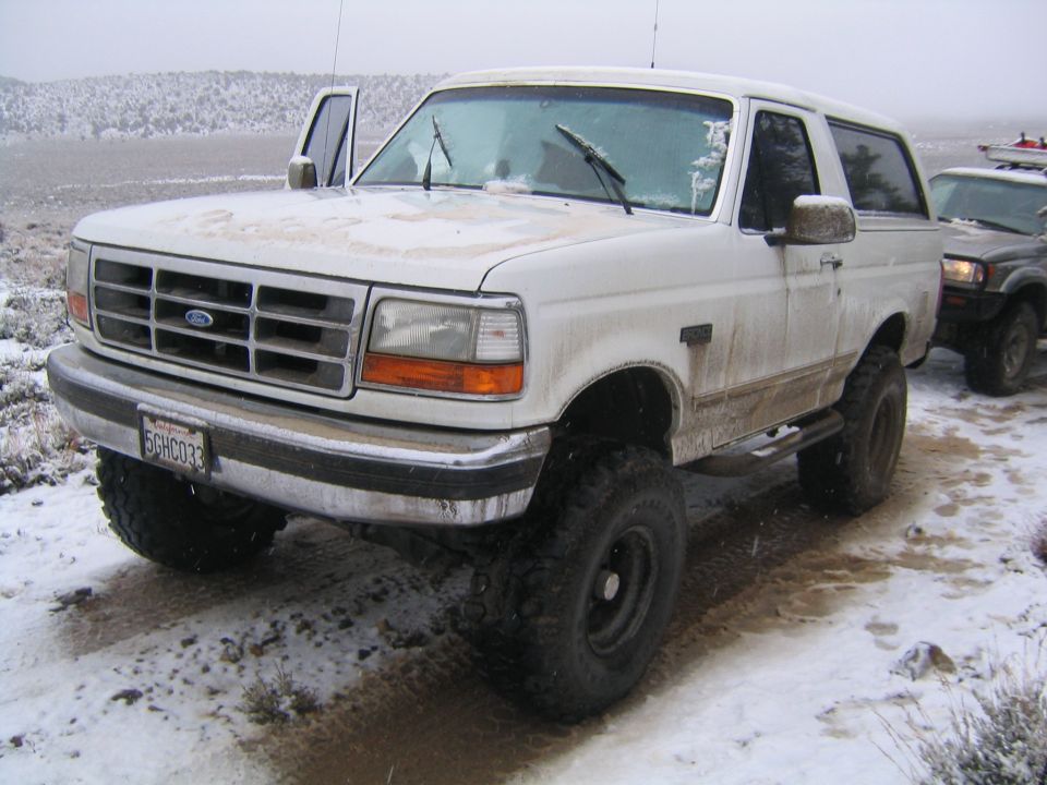 Snow-covered white lifted Ford Bronco on desert road, 3/4 front view with black steel wheels