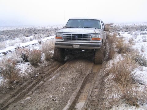 1993 Ford Bronco - A white 1993 Ford Bronco navigates a muddy and snowy trail, its off-road capabilities.