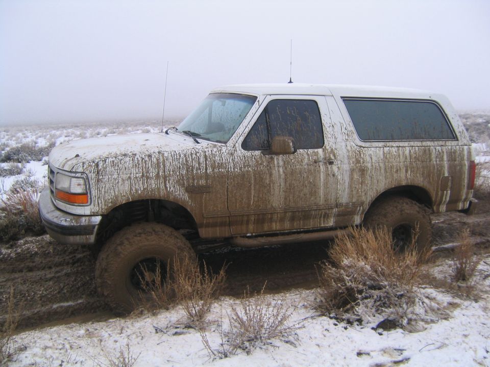 Mud-caked white two-door SUV with lift and big tires in snowy field