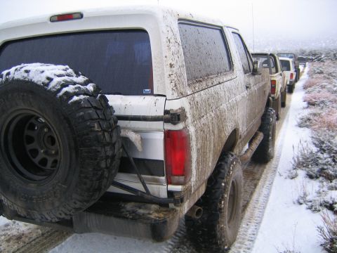 1993 Ford Bronco - A convoy of muddy SUVs, including a 1993 Ford Bronco, travels down a snowy road.