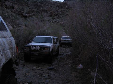 1993 Ford Bronco - Two vehicles navigate a rocky, overgrown trail in a desert canyon.