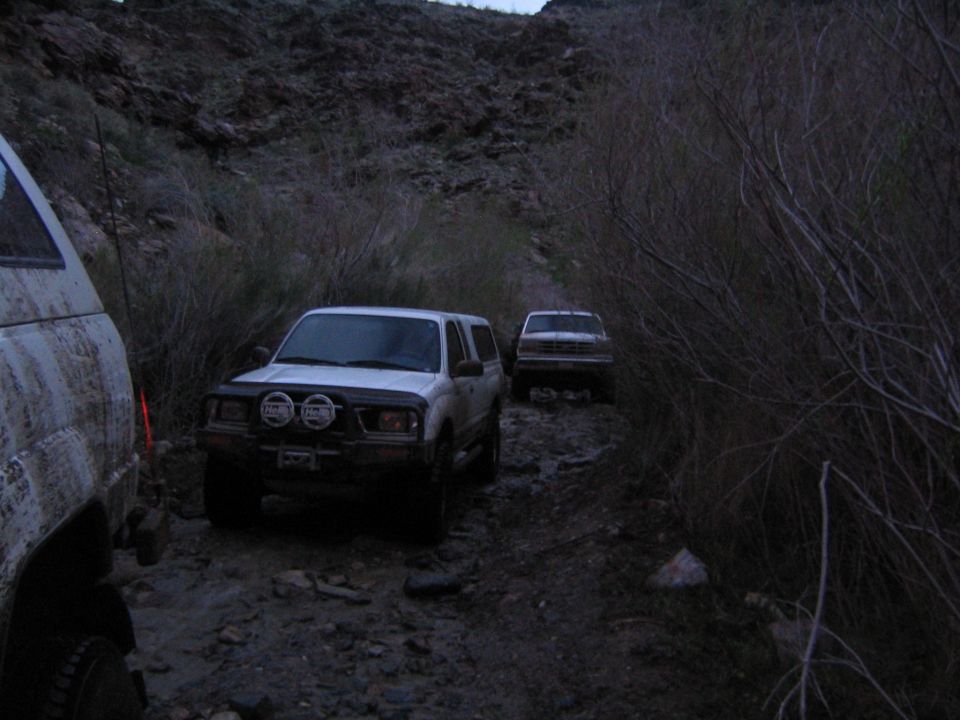 White off-road SUVs on a rocky muddy canyon trail at dusk