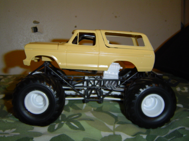 Yellow 1979 Ford Bronco model with oversized tires and exposed engine, viewed from the side