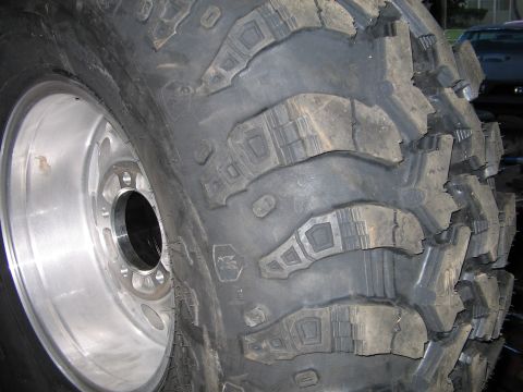 1978 Ford Bronco - A close-up view of a off-road tire mounted on a shiny aluminum wheel, showing its deep tread blocks.