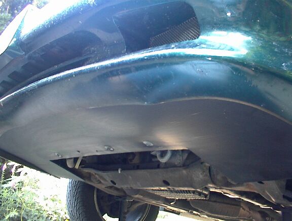 Black plastic lower cowling air dam bolted under the front bumper of a dark green car