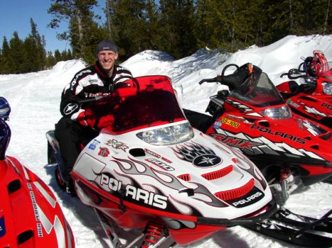 2003 Polaris 600 PRO X - A man poses on a Polaris snowmobile in a snowy landscape with other snowmobiles nearby.