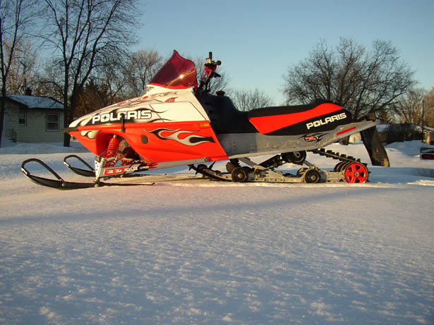 Red and black Polaris snowmobile parked on snow, side view