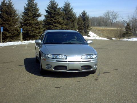 2002 Oldsmobile Aurora - Front view of a silver 2002 Oldsmobile Aurora parked in a lot with trees in the background.