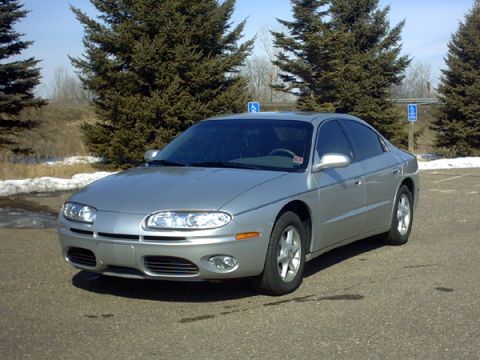 2002 Oldsmobile Aurora - Silver sedan parked in a lot with trees and snow in the background.