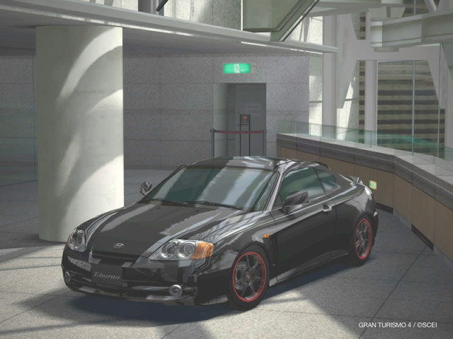 Black Hyundai Tiburon coupe with red-lip wheels parked in a modern glass-walled atrium
