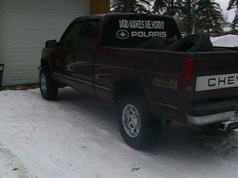 1981 Chevrolet C/K Pickup - A dark red pickup truck is parked in the snow, a humorous sticker on its rear window.