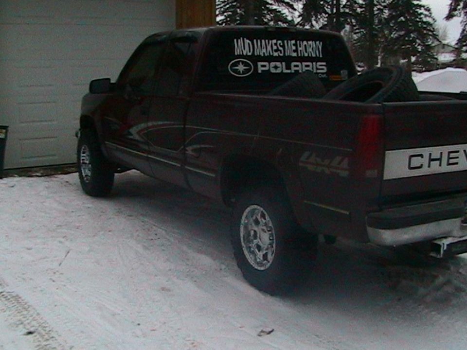 Side view of a dark red pickup truck with a "MUD MAKES ME HORNY POLARIS" sticker
