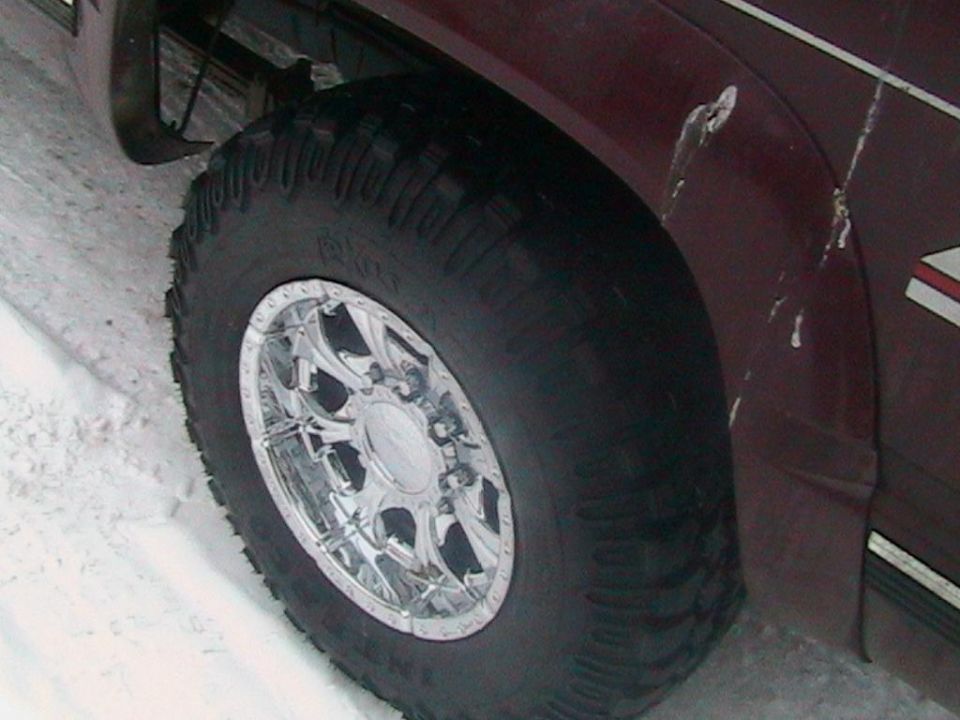 close-up of a large off-road tire on a maroon truck with chrome rims, in snow