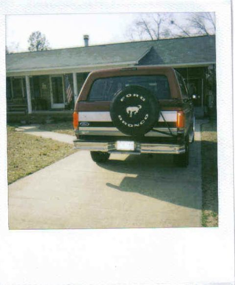 1995 Ford Bronco - The rear of a Ford Bronco is shown parked in front of a house, a spare tire mounted on the tailgate.