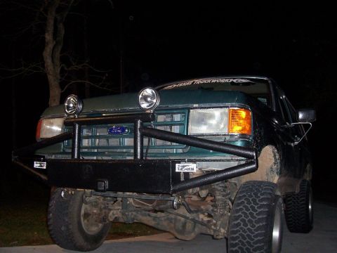 1989 Ford Bronco - Front view of a green Ford truck with a custom bumper and auxiliary lights, parked at night.