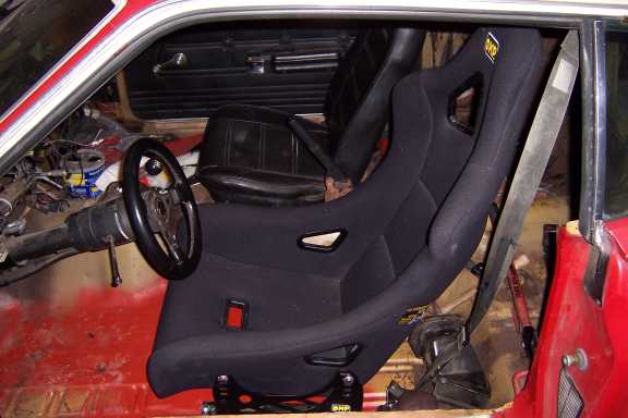 Red car interior with a black OMP racing bucket seat and small aftermarket wheel.