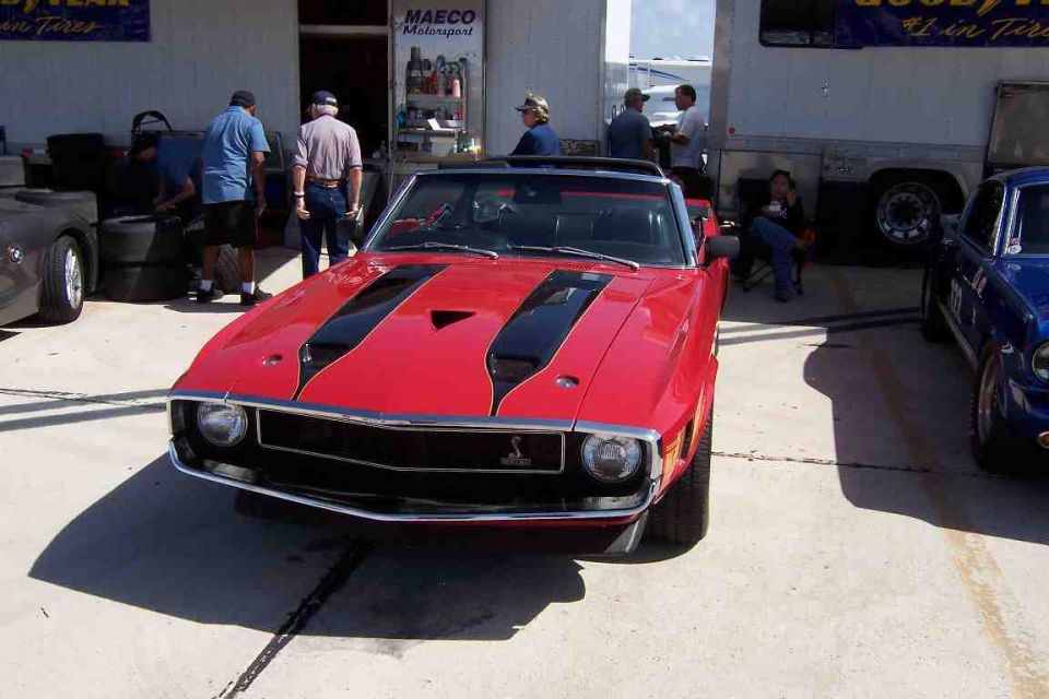 Red convertible muscle car with black stripes on hood, parked next to a blue car