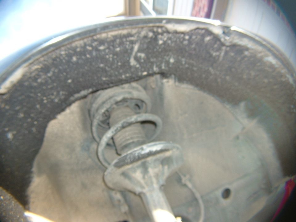 Coil spring and strut assembly seen inside a dusty wheel well with the wheel removed