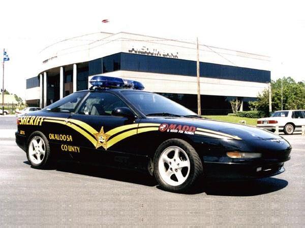 Black Okaloosa County Sheriff Ford Probe coupe with gold graphics and roof light bar, front three-quarter view