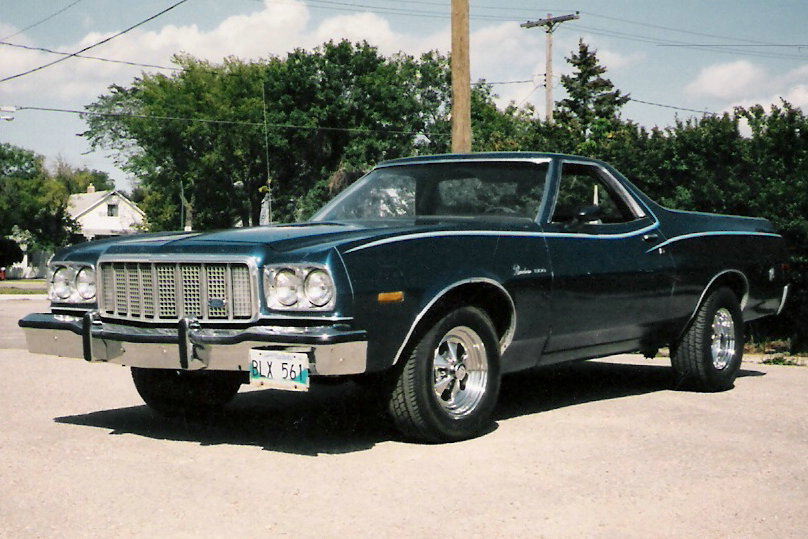 Dark blue 1976 Ford Ranchero, front three-quarter view, chrome grille and mag wheels, parked on gravel