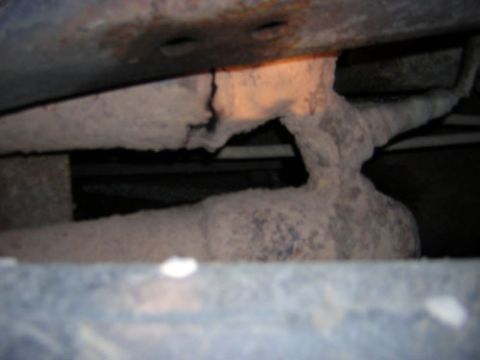 1995 Ford Bronco - Close-up view of a heavily rusted exhaust pipe and vehicle frame components.