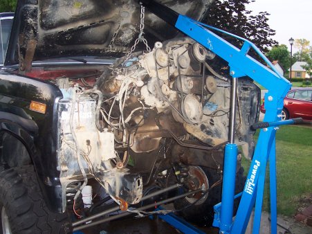 1986 Ford Bronco - Engine hoist lifting the engine out of a black vehicle. The Supermotors.net logo is visible at the bottom of the image.