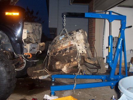 1986 Ford Bronco - An engine is being removed from a vehicle using a blue engine hoist.