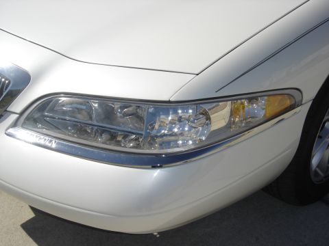 1997 Lincoln Mark VIII - Close-up of the front corner of a white 1997 Lincoln Mark VIII, highlighting the headlight assembly with chrome accents.