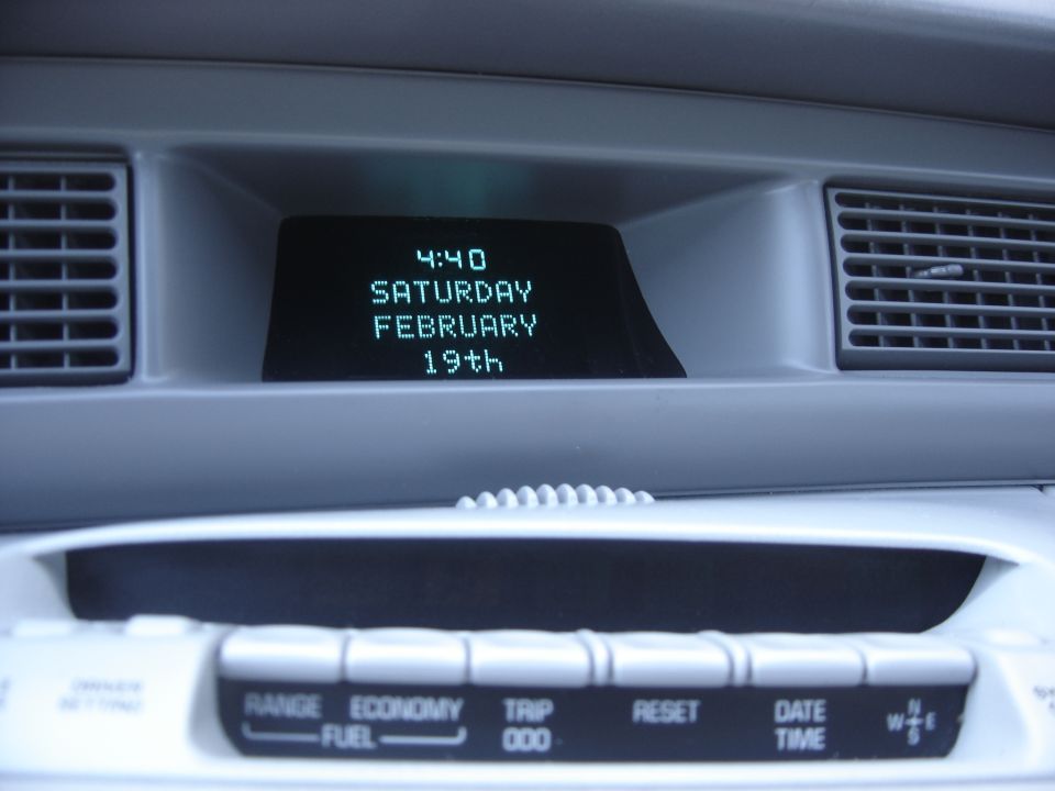 Car dashboard showing digital clock and calendar display, with climate control buttons below