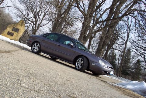 1996 Ford Taurus - A 1996 Ford Taurus sedan is seen from a 3/4 front angle on a sloped road with winter scenery.