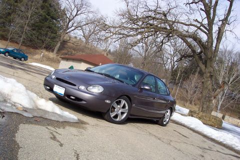 1996 Ford Taurus - A 1996 Ford Taurus is parked on a street, with snow visible on the ground and another car in the distance.