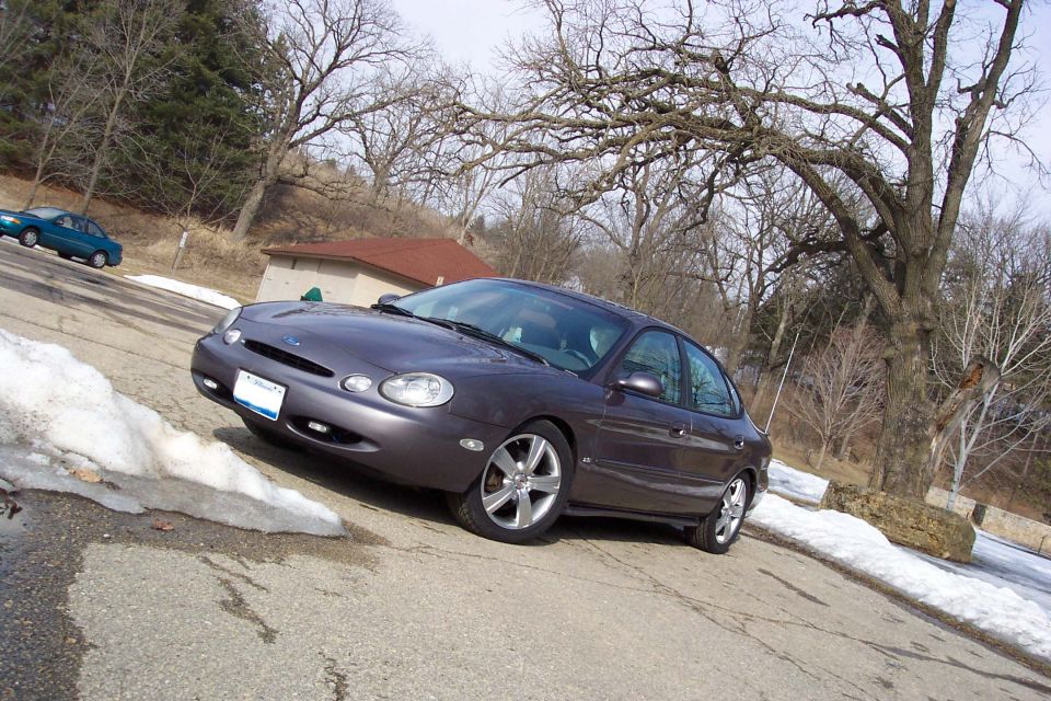 1996 Ford Taurus parked on a street with snow on the side, another car in the background