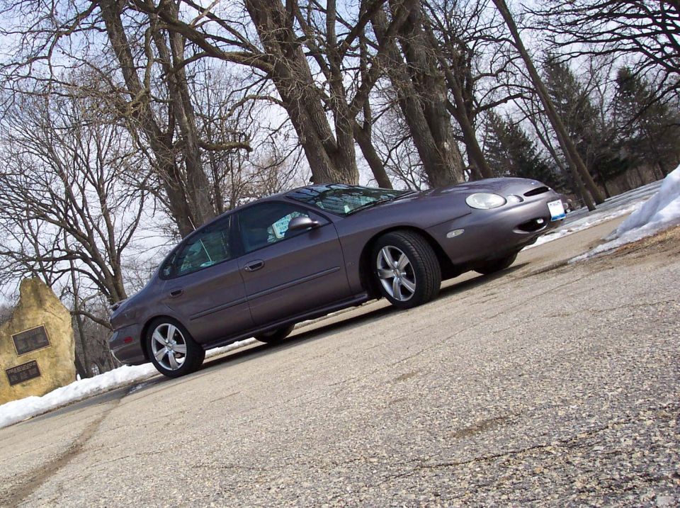 Gray Ford Taurus parked on a road with trees and snow in the background