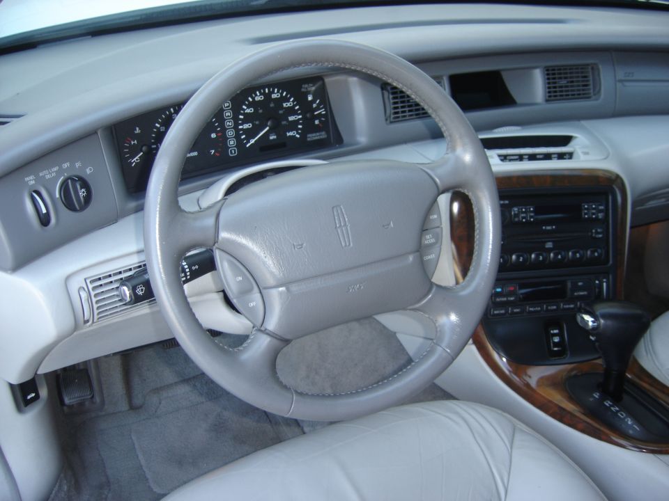 Car interior with gray leather seats, wood trim, and a Lincoln emblem on the steering wheel