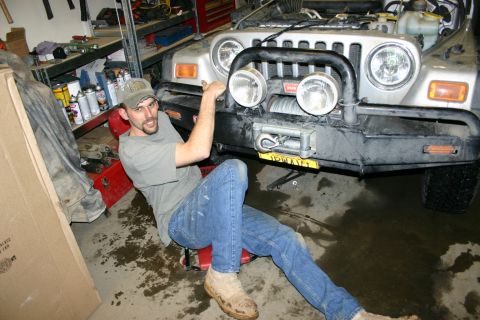2003 Jeep TJ - A man works on the front end of a silver 2003 Jeep TJ, which is equipped with a winch and extra lights.