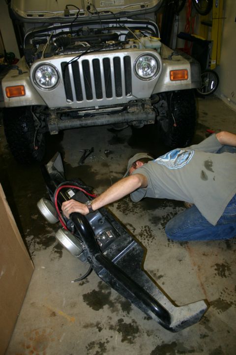 2003 Jeep TJ - Person working on a Jeep TJ, holding the front bumper with lights.