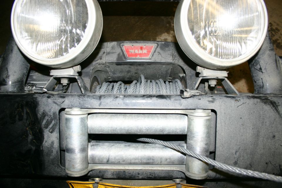 Close-up of a WARN winch and two large auxiliary lights mounted on a vehicle's front bumper