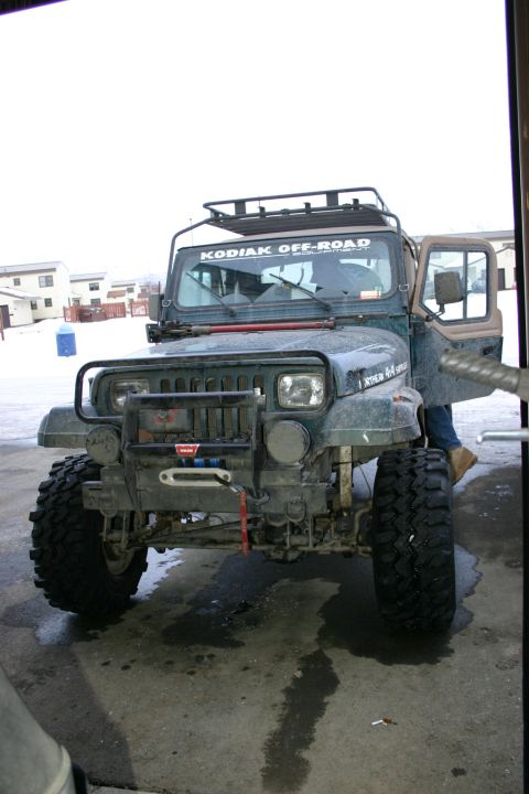 2003 Jeep TJ - This modified Jeep Wrangler YJ is parked outdoors with its driver's side door open, revealing a person inside.