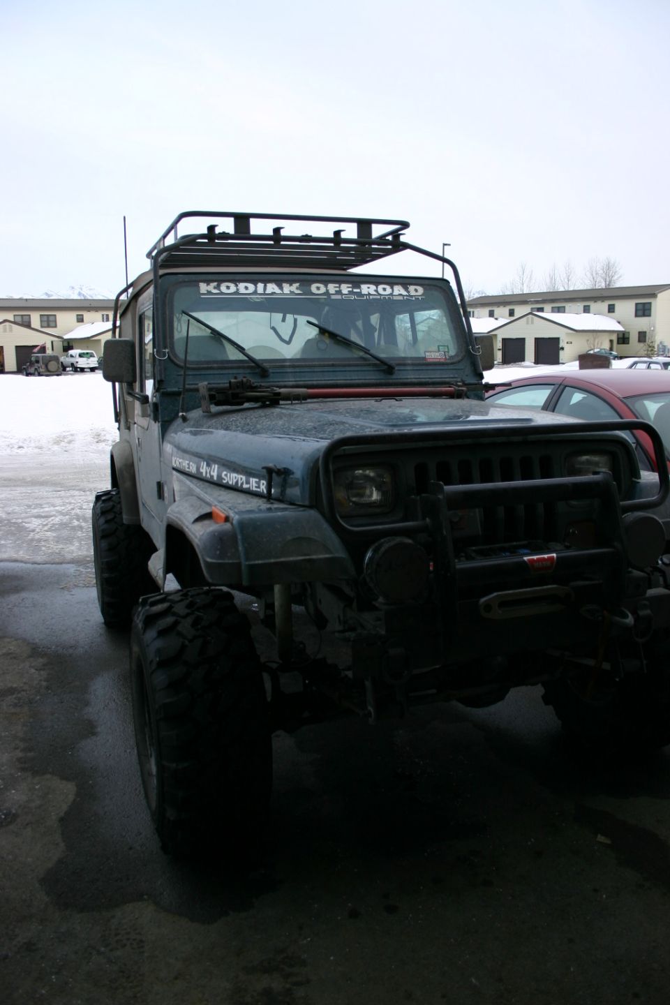 Dark green Jeep Wrangler with a roof rack and "KODIAK OFF-ROAD" sticker, seen from a 3/4 front angle