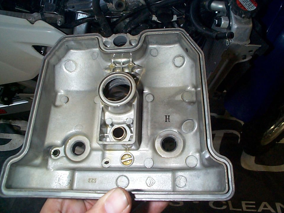 Underside of an aluminum motorcycle valve cover held in hand during valve work