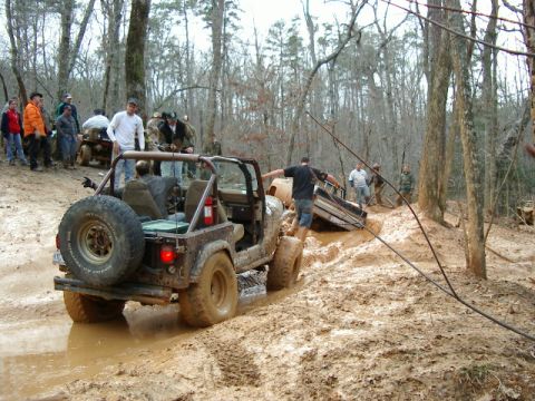 1985 Ford Bronco - Off-roaders attempt to free a stuck Jeep Wrangler and another vehicle from deep mud in a wooded area.