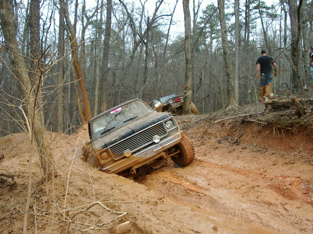 Muddy lifted square-body 4x4 SUV climbing a rutted red clay off-road trail