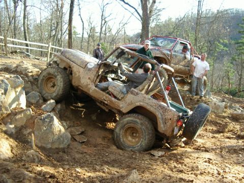1985 Ford Bronco - Two off-road vehicles are stuck in mud and rocks on a wooded trail.