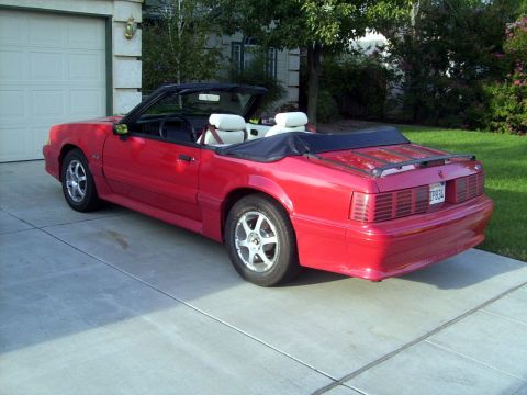 1978 Ford Mustang II - This red convertible is parked in front of a garage with the top down, revealing its white interior.