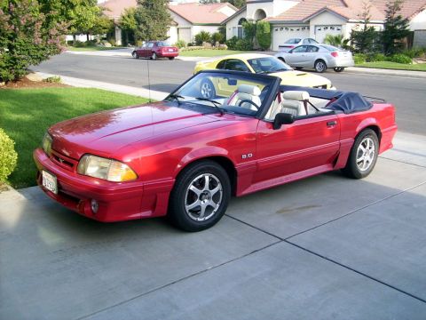 1978 Ford Mustang II - A red convertible with a white interior is parked on a driveway, with other vehicles in the background.