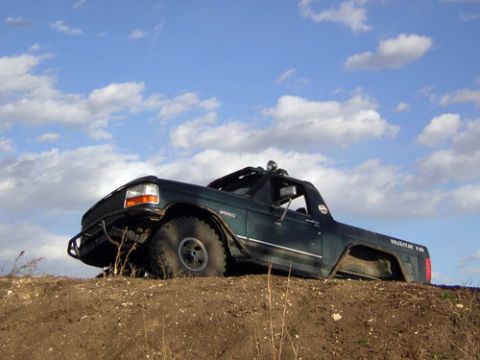 1995 Ford Bronco - Dark green 1995 Ford Bronco with custom bumper and lights sits on a dirt hill.